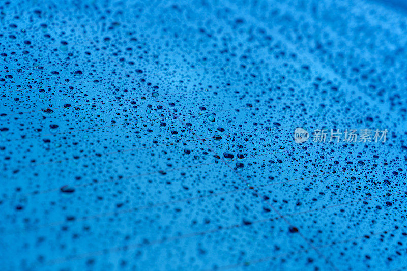 A full-frame shot capturing the intricate textures formed by water droplets on the rear car windshield as the background